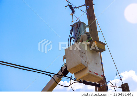 Technician works safely from bucket lift to install service electrical equipment attached to tall pole. Technician works safely from bucket lift to install service electrical equipment attached to tall pole. 120491442