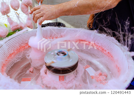 Pink cotton candy being made outdoors using machine pan for preparing delicious treat Pink cotton candy being made outdoors using machine pan for preparing delicious treat 120491443