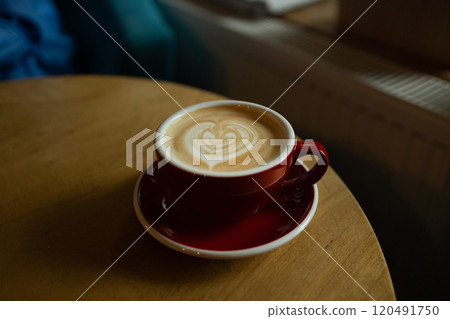 Close up with hot cappuccino with coffee art on the wooden table.A red cup of latte art coffee on natural wood table. Close up with hot cappuccino with coffee art on the wooden table.A red cup of latte art coffee on natural wood table. 120491750