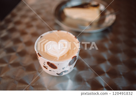 Chocolate cup of cappuccino and cake on a table in the cafe terrace outside. Atmospheric coffee time. Heart shaped dessert decorations 120491832