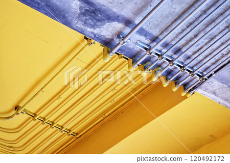 Electric metal pipe on raw and yellow concrete ceiling. 120492172