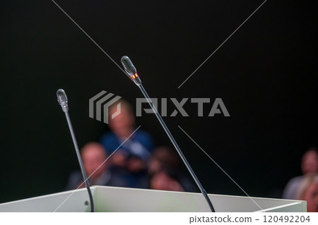 Microphones set up for public speaking event with audience blurred 120492204