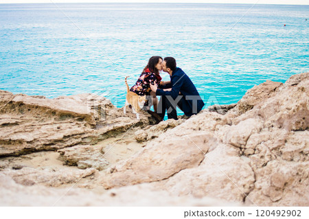 a young couple in love playing with orange stray cat on fabulous rocky coast with turquoise water Ayia Napa, Cyprus 120492902