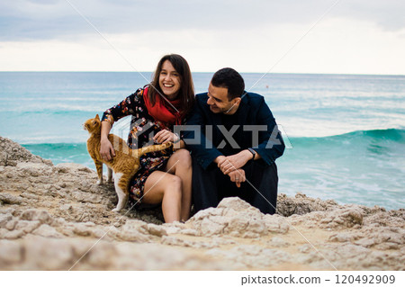a young couple in love playing with orange stray cat on fabulous rocky coast with turquoise water Ayia Napa, Cyprus a young couple in love playing with orange stray cat on fabulous rocky coast with turquoise water Ayia Napa, Cyprus 120492909