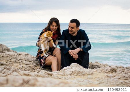 a young couple in love playing with orange stray cat on fabulous rocky coast with turquoise water Ayia Napa, Cyprus a young couple in love playing with orange stray cat on fabulous rocky coast with turquoise water Ayia Napa, Cyprus 120492911