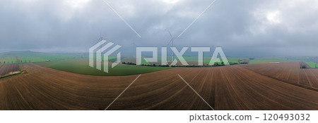 A drone panorama of wind turbines on farmland partially obscured by low-hanging clouds on a misty day 120493032