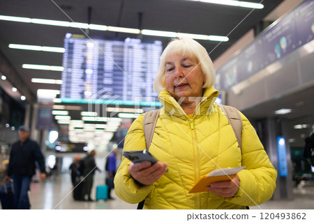 Traveler tourist happy smiling joyful fun mature elderly senior lady woman 55 years old with hand luggage, backpack holds passport and waits for flight travel at international airport terminal.  120493862