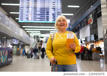 Traveler tourist happy smiling joyful fun mature elderly senior lady woman 55 years old with hand luggage, backpack holds passport and waits for flight travel at international airport terminal.  120493870