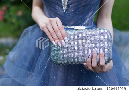 Close-up of a woman wearing a formal light blue dress, her hands with an attractive manicure, holding a glittering handbag. Selective focus. 120493919
