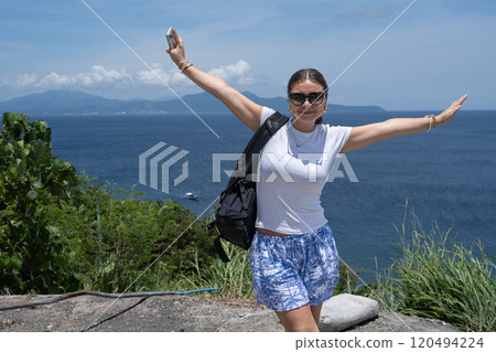 A smiling teenage girl wearing sunglasses and holding her arms out in front of an ocean view A smiling teenage girl wearing sunglasses and holding her arms out in front of an ocean view 120494224