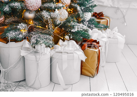 Wrapped holiday gift boxes under beautifully decorated Christmas tree with white and gold ornaments Wrapped holiday gift boxes under beautifully decorated Christmas tree with white and gold ornaments 120495016
