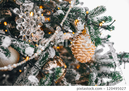 Snowy Christmas tree branch with festive lights and decorative gold and silver ornaments close up Snowy Christmas tree branch with festive lights and decorative gold and silver ornaments close up 120495027