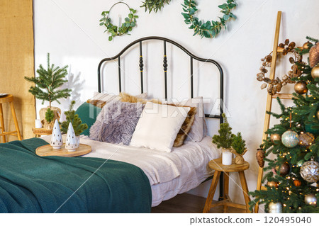 Christmas tree in cozy bedroom decorated for holidays with bad with plush pillows and green blanket 120495040