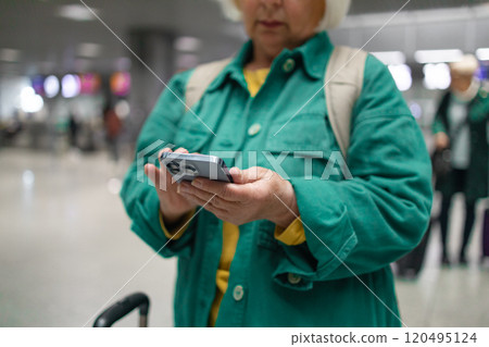 Caucasian 60s smiling business woman in green jacket in international airport, checking her phone while waiting for her flight Caucasian 60s smiling business woman in green jacket in international airport, checking her phone while waiting for her flight 120495124