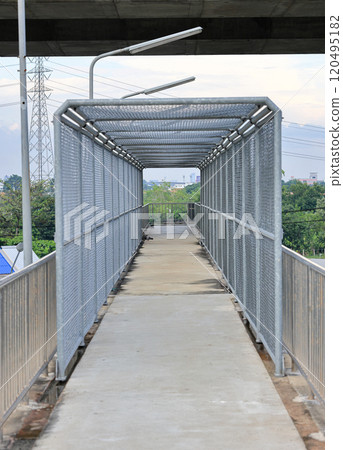 Metal mesh on steel walkways or caged in walkway over passing highway and railway. Metal mesh on steel walkways or caged in walkway over passing highway and railway. 120495182