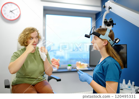 A young woman at an appointment with an otolaryngologist talks about her symptoms. A professional ENT doctor examines a patient. 120495331