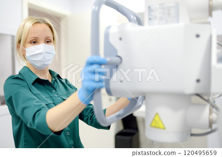 Female technician adjusts X-Ray machine. Female radiologist is going to take an Xray of patient in X-ray room of modern clinic. Female technician adjusts X-Ray machine. Female radiologist is going to take an Xray of patient in X-ray room of modern clinic. 120495659