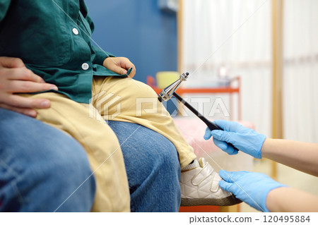 Baby and his mother are being seen by a pediatric neurologist in a modern medical clinic. Doctor conducts tests, checks the reflexes using neurological hammer of small patient. Highly qualified cure 120495884