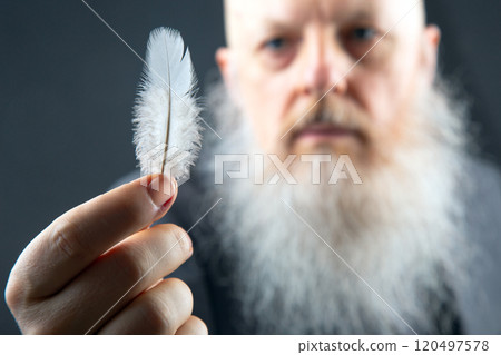 an aged man with a full white beard focuses on a single delicate feather 120497578
