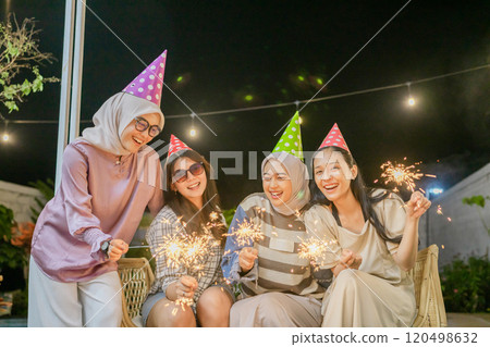 Friends joyfully celebrate at night with colorful sparklers and party hats 120498632
