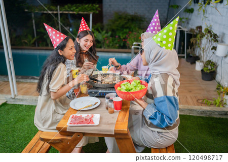 Friends celebrating with barbecue and colorful party hats at an outdoor gathering 120498717