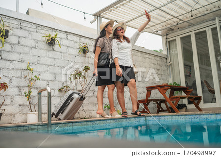 Friends Enjoying a Relaxing Time by the Poolside with Luggage and a Smartphone 120498997
