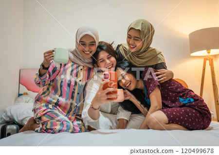 Friends joyfully taking a selfie in a cozy bedroom, sharing precious memories 120499678