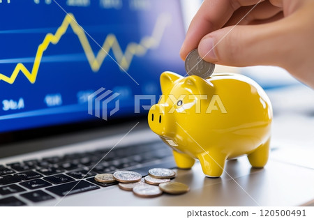 Saving strategies: hand puts crypto coin into yellow piggy bank with financial graph in background 120500491