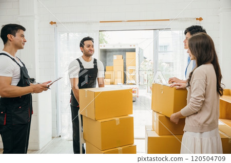 Before signing moving documents family inspects checklist boxes. Worker holds a box. Professional movers ensure precise relocation service. Teamwork and home relocation evident. Movind Day Before signing moving documents family inspects checklist boxes. Worker holds a box. Professional movers ensure precise relocation service. Teamwork and home relocation evident. Movind Day 120504709