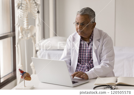Older Indian cardiologist working on laptop in office Older Indian cardiologist working on laptop in office 120505578