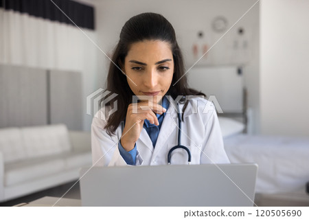 Close up of thoughtful Brazilian doctor using laptop at workplace 120505690
