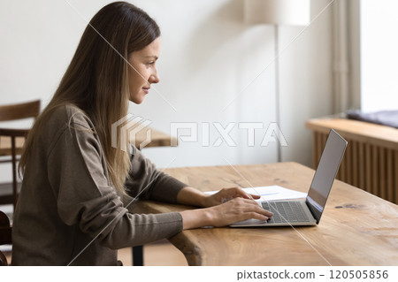 Side view focused woman sitting at table, working on laptop 120505856