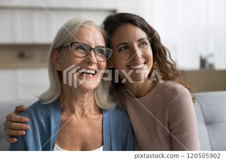 Dreamy pensive young woman hugging older mother smile looking away 120505902