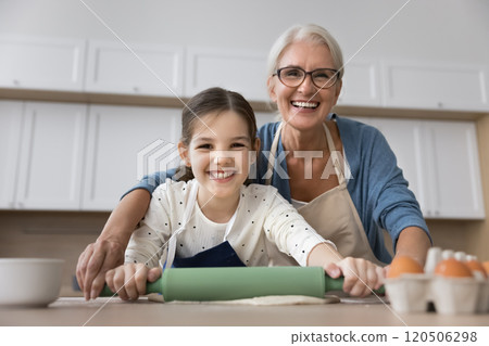 Portrait of grandmother and granddaughter flattening dough together Portrait of grandmother and granddaughter flattening dough together 120506298