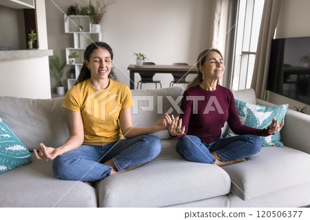 Positive senior Hispanic mom and daughter meditating with closed eyes 120506377