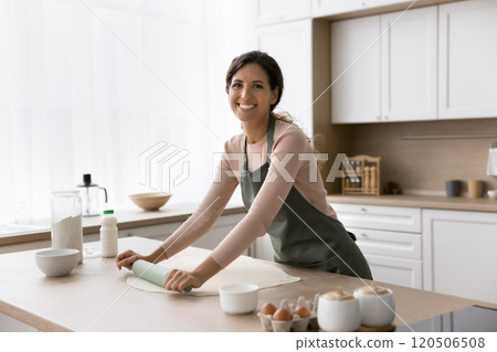 Beautiful young woman wearing apron rolling out homemade dough Beautiful young woman wearing apron rolling out homemade dough 120506508