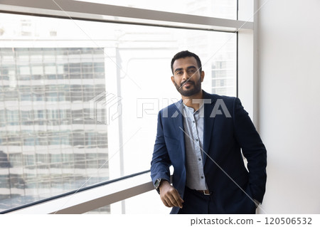Positive confident young Indian manager man standing at office window Positive confident young Indian manager man standing at office window 120506532