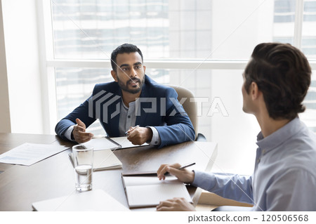 Serious confident Indian business owner man talking to male coworker Serious confident Indian business owner man talking to male coworker 120506568