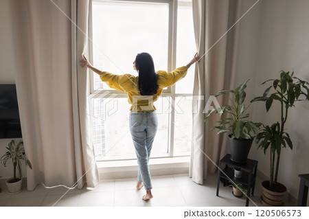 Beautiful black haired young woman standing at large window Beautiful black haired young woman standing at large window 120506573