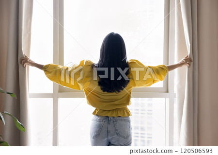 Back of young woman in casual clothes opening drapes 120506593