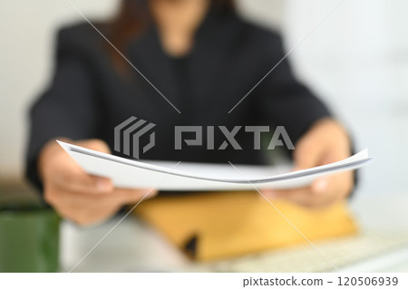 Close up of female manager sitting a office desk extending documents towards the camera Close up of female manager sitting a office desk extending documents towards the camera 120506939
