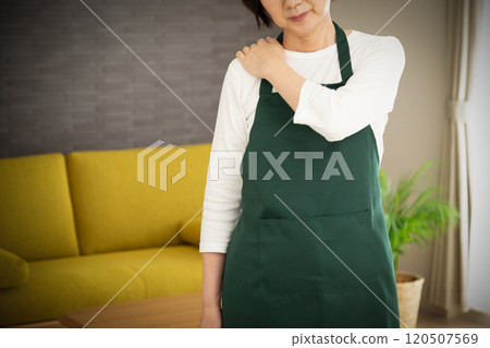 A middle-aged woman wearing an apron suffering from stiff shoulders 120507569