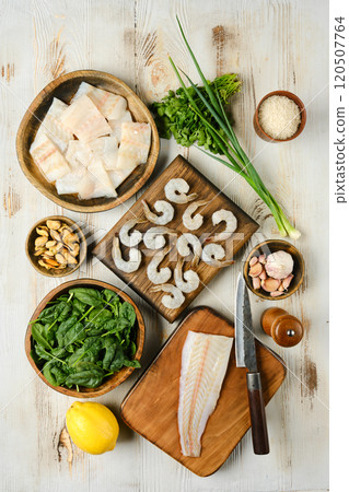 Fresh seafood and vegetables arranged on a wooden table for meal preparation in a bright kitchen 120507764