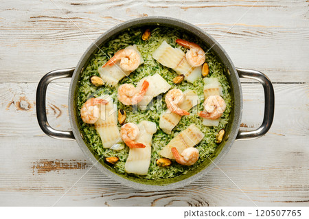Delicious shrimp and fish rice dish prepared in a gray pot with green herbs on a wooden table Delicious shrimp and fish rice dish prepared in a gray pot with green herbs on a wooden table 120507765
