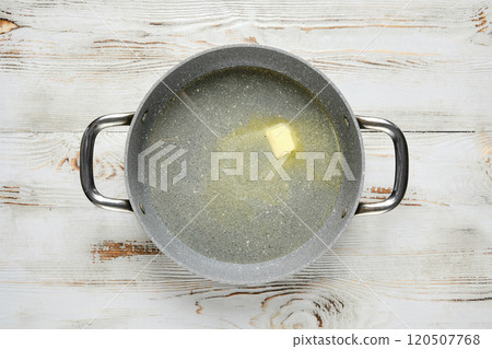 Top view of a piece of butter melts in a pan on a wooden table 120507768