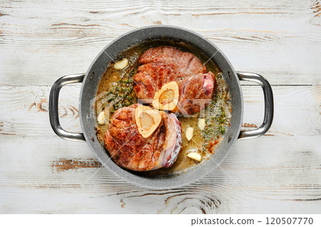 Two pieces of beef meat are seared in a pan with garlic and herbs Two pieces of beef meat are seared in a pan with garlic and herbs 120507770