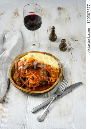 Beef stew with mashed potatoes, onions, and carrots on a white table, with red wine 120507777