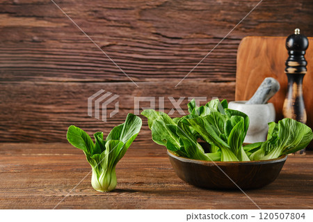 Fresh bok choy in a rustic kitchen setting with wooden background and cooking utensils 120507804