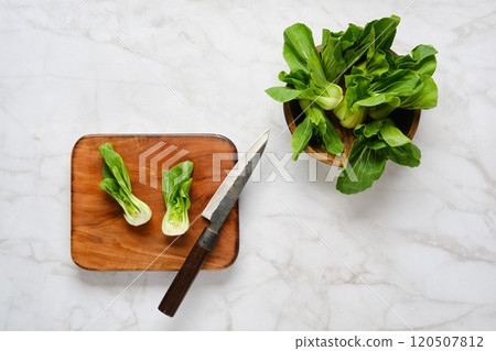 Preparing fresh bok choy on a wooden cutting board with a knife and additional greens nearby 120507812