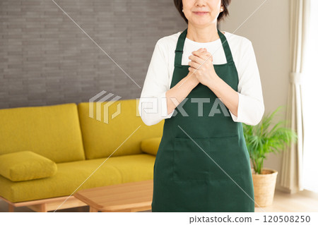 一位穿著圍裙的中年婦女家庭主婦在自家客廳開心地玩耍。 一位穿著圍裙的中年婦女家庭主婦在自家客廳開心地玩耍。 120508250